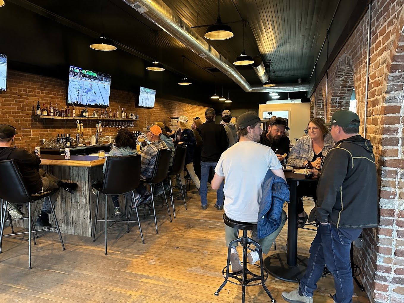 People socializing in a bar with TV screens.