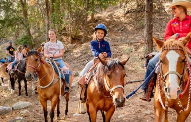 A family horseback riding in the forest, with the instructor and the youngest child in the foreground