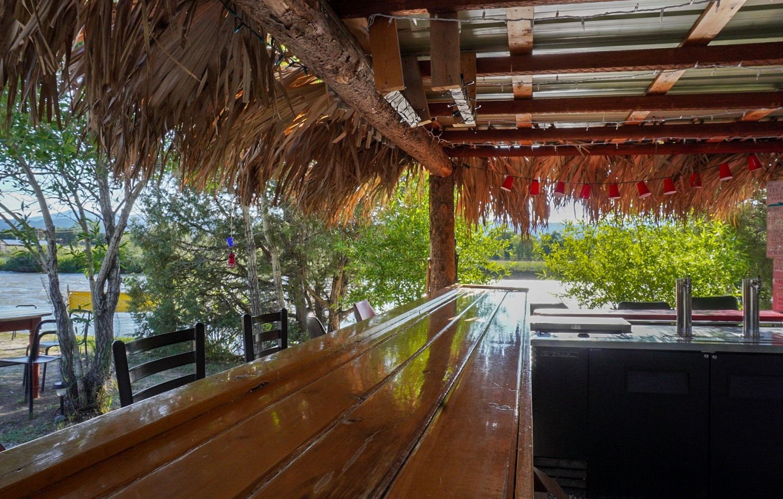 Outdoor tiki bar by riverside with thatched roof.