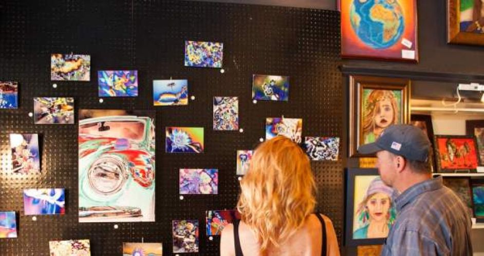 Two people turned away from the camera viewing a wall of various small art pieces