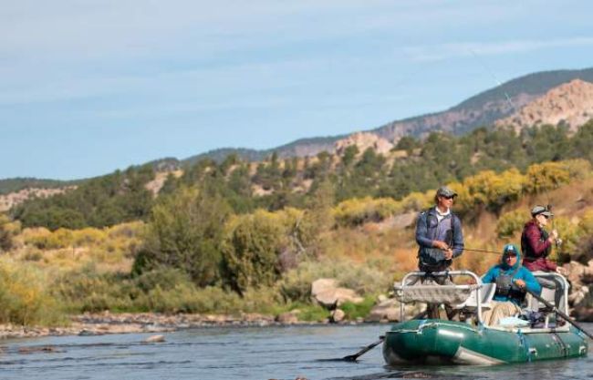 Three people fishing from a raft in Buena Vista, in front of mountains and low brush
