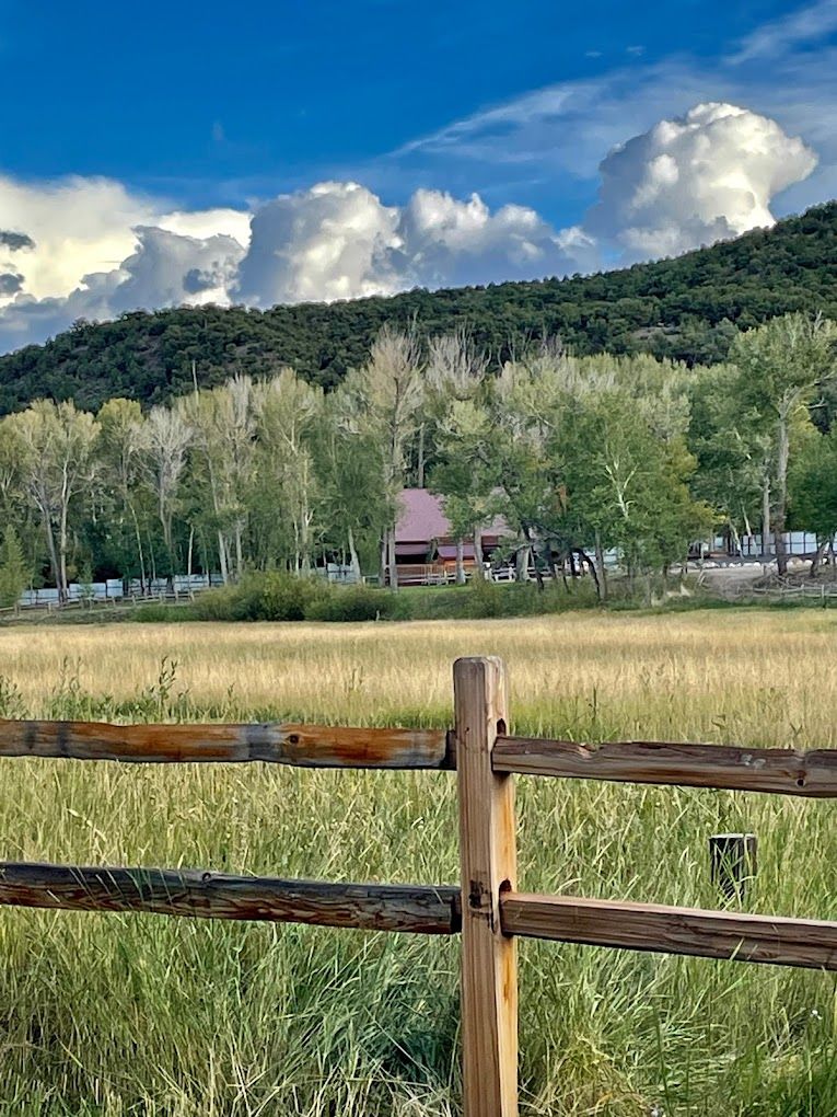 Wooden fence with house, trees, and mountains background.