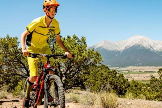 A man mountain biking on a trail, with the Sangre de Cristo Mountains in the background